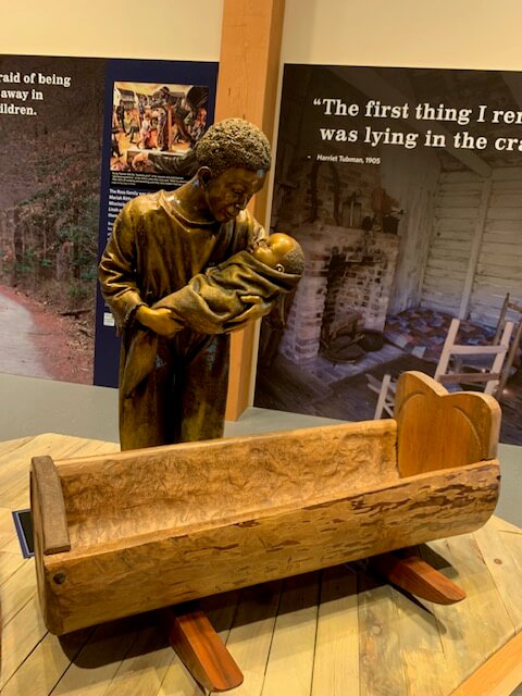 Slave woman holding baby near carved wooden cradle