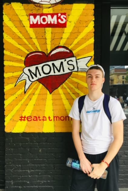 Young guy standing next to Mom's Restaurant sign in NYC